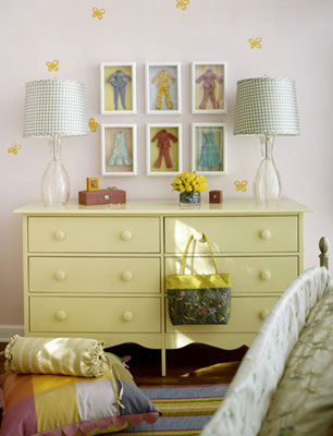 A yellow dresser with boll dress-up clothes in frames above it