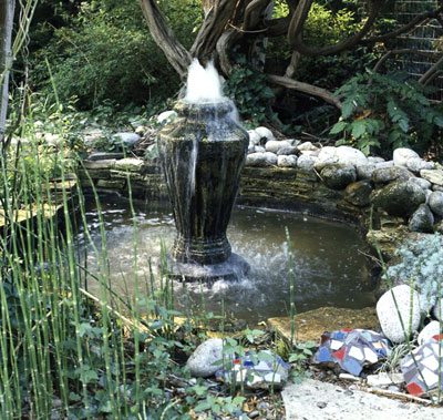 Large basin fountain in the middle of a backyard pond surrounded by rocks