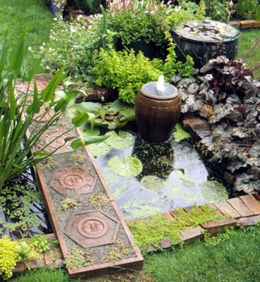 A small pot fountain surrounded by lilypads in a brick-lined pond